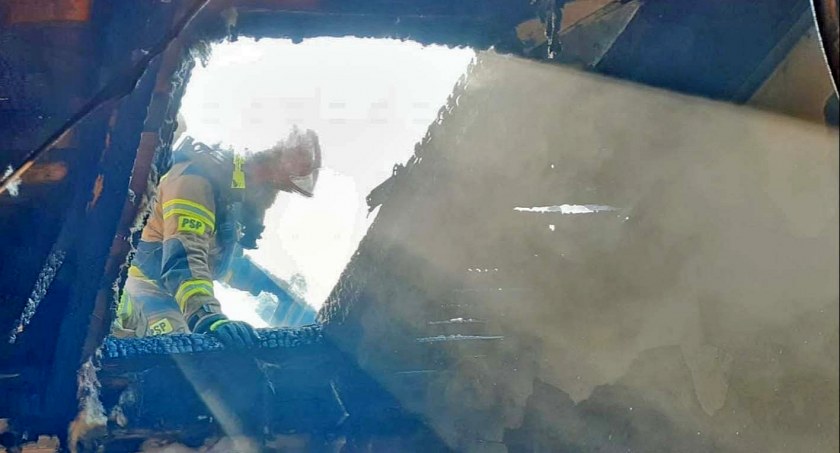 Zdjęcie strażaka, który gasi poddasze wodą podawaną przez wypalone okno