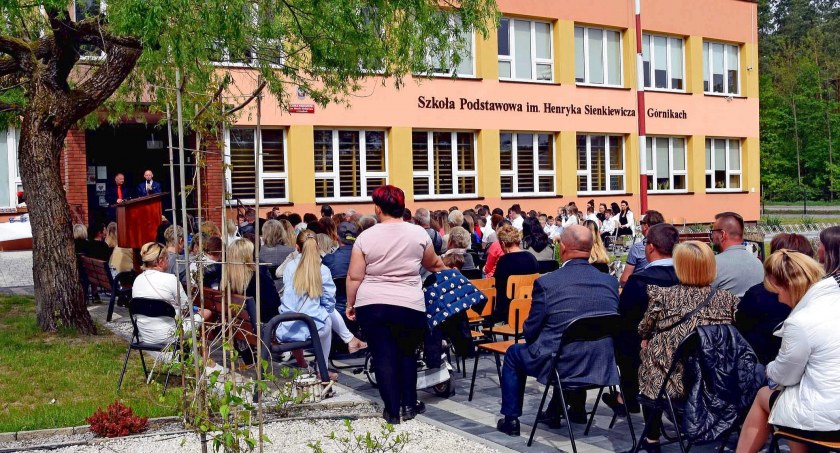 Zdjęcie uczestników uroczystości przed Szkołą Podstawowa w Górnikach. Na frontonie imię patrona szkoły