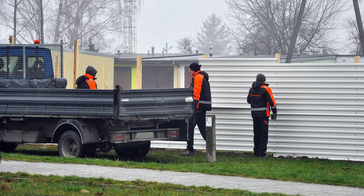 Zdjęcie pracowników, którzy grodzą płotem z blachy plac budowy domów komunalnych w Końskich