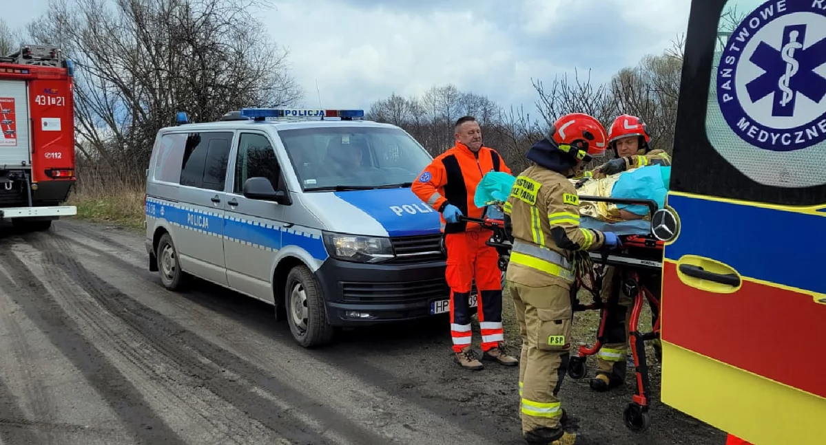 Zdjęcie strażaków, którzy po wydobyciu człowieka pomagają w umieszczeniu w karetce pogotowia