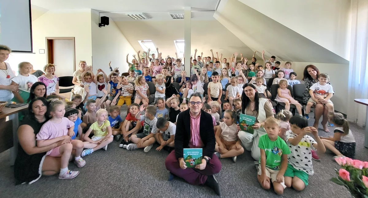 Zdjęcie Wojciecha Purtaka wśród dzieci na spotkaniu w smykowskiej bibliotece