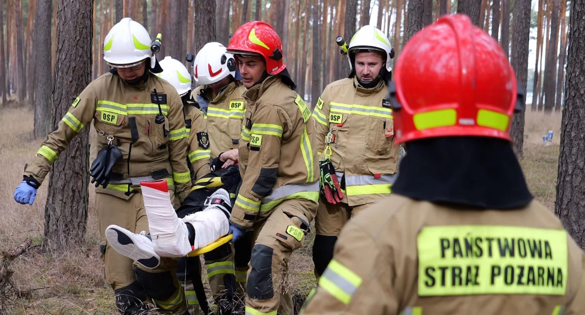 Zdjęcie strażaków, którzy transportują na noszach rannego harcerza
