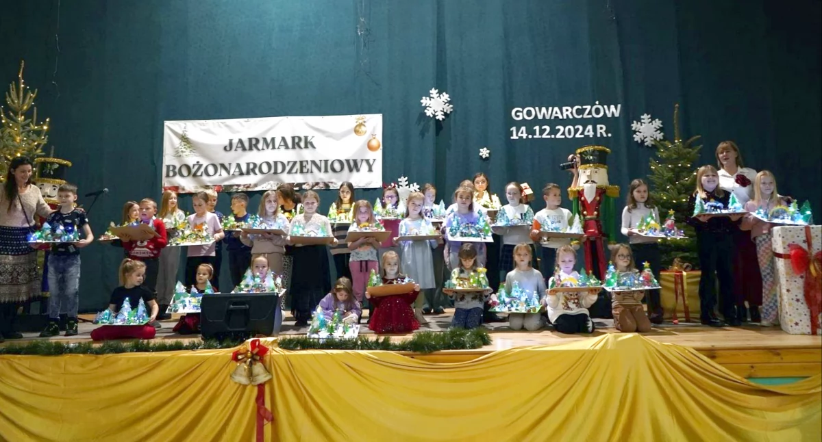 Zdjęcie dzieci z własnoręcznie wykonanymi ozdobami choinkowymi oraz organizatorami jarmarku w Gowarczowie
