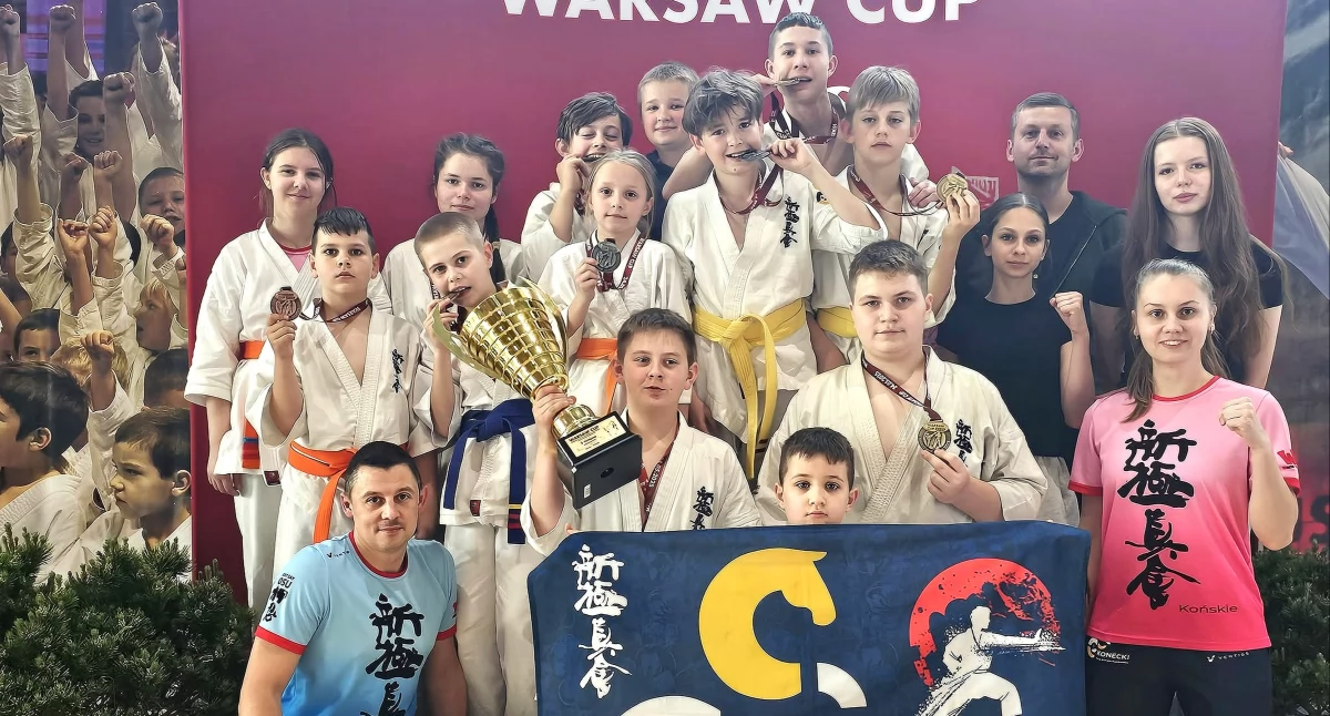 Zdjecie zawodników Koneckiego Klubu Karate Kyokushin z trenerem Mateuszem Garbaczem i trofeami turnieju Warsaw Cup 2025