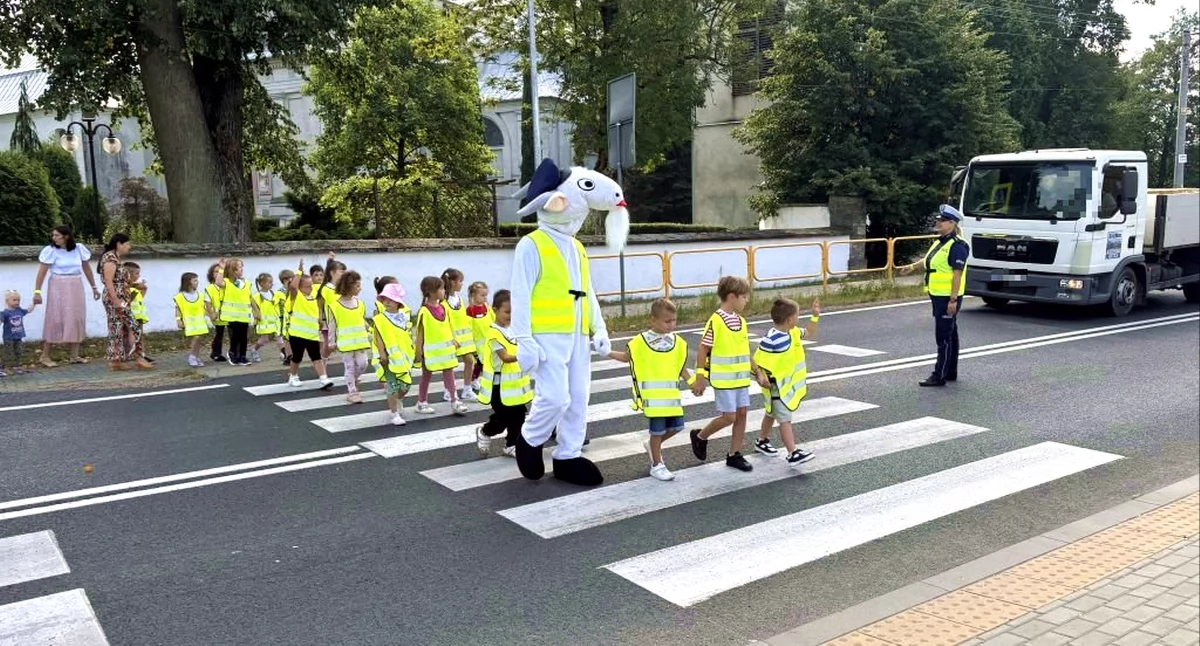 Zdjęcie policjantki z drogówki i koziołka Spoko, którzy instruują dzieci, jak przechodzić przez ulicę