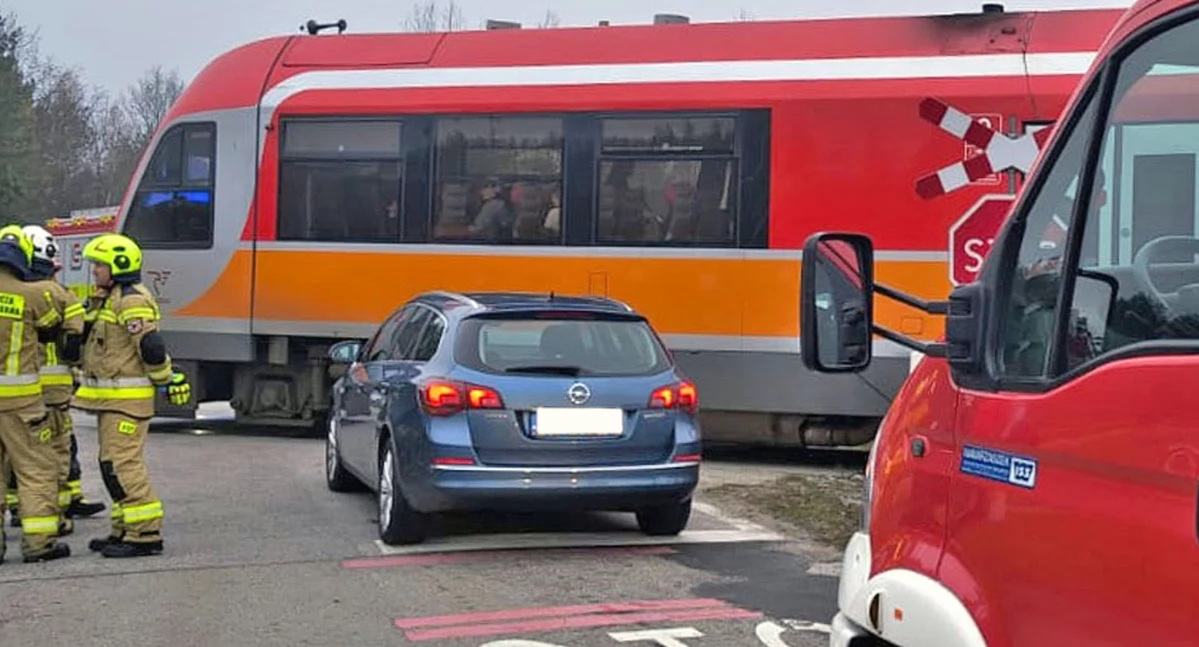 Zdjęcie niewiele uszkodzonego opla stojącego między pociągiem a wozem strażackim