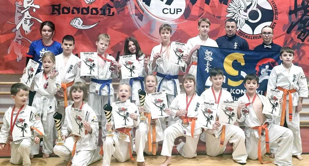 Zdjęcie młodych zawodników Koneckiego KKK z trenerem Mateuszem Garbaczem i trofeami wywalczonymi w Radomsku