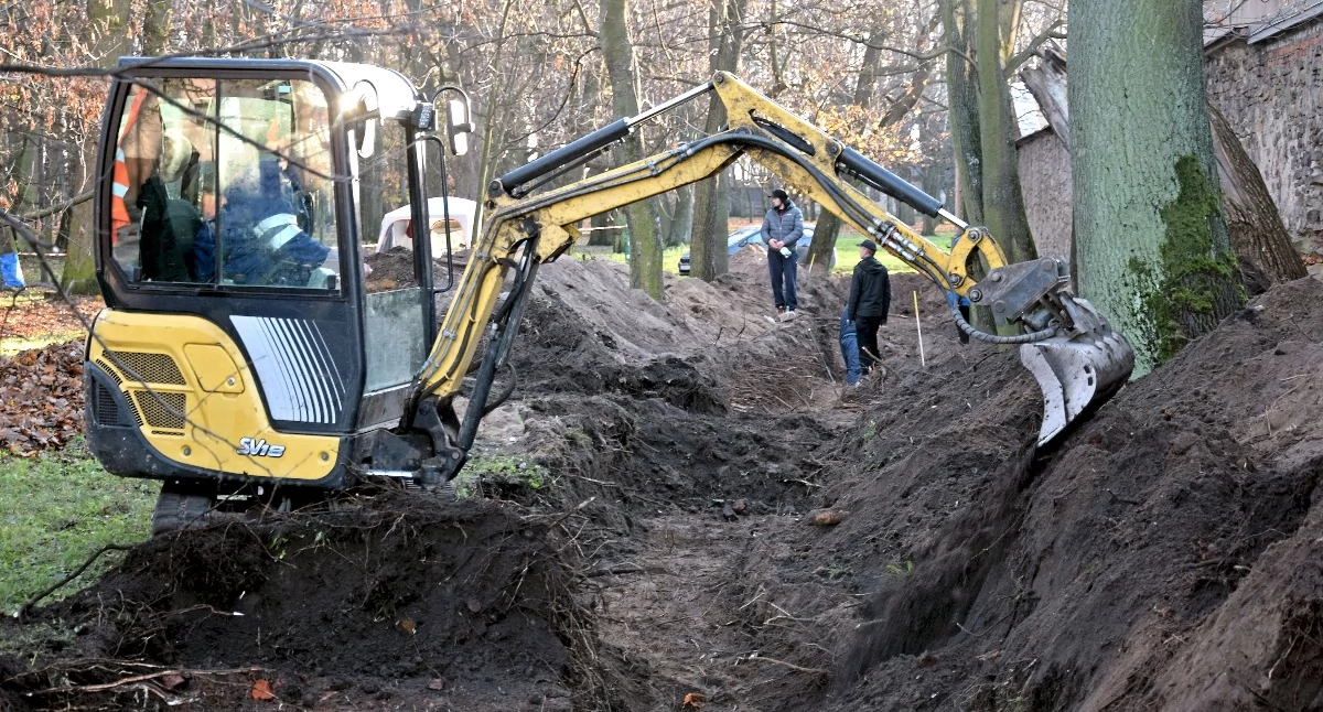 Zdjęcie koparki, która odsłania ziemię między murem dawnego UB, a koneckim parkiem